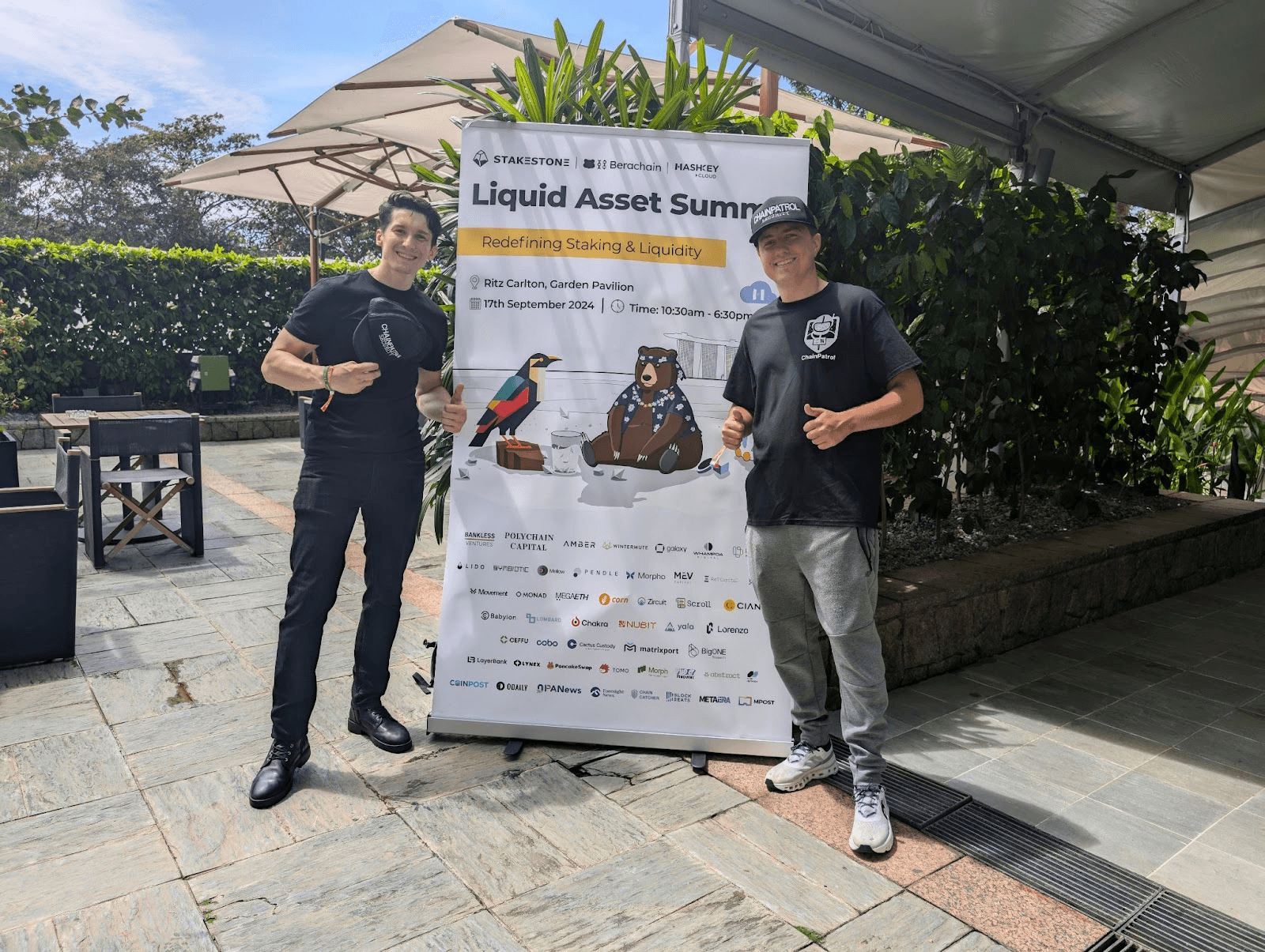 two men wearing black standing next to a sign at TOKEN2049 in singapore