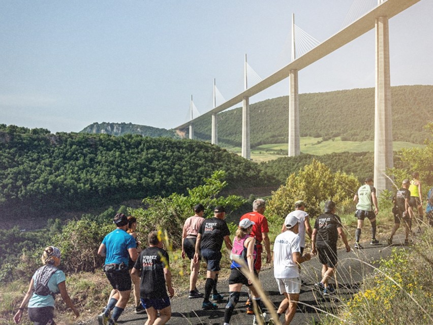 Des participants courant sur un sentier avec un grand pont à câbles en arrière-plan.