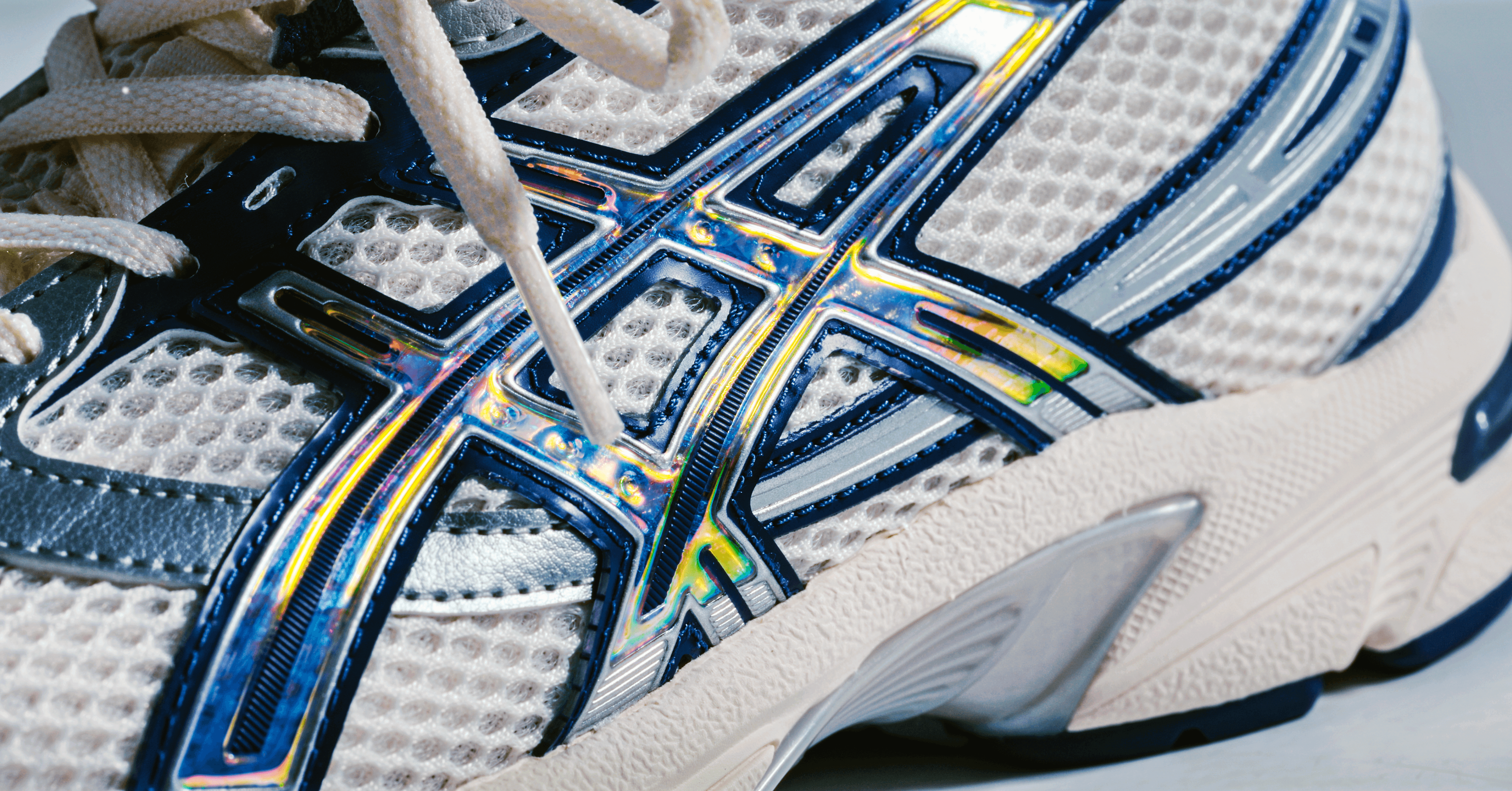 Close-up of a white and blue athletic running shoe featuring a textured mesh design and iridescent detailing, showcasing the intricate patterns and modern style.