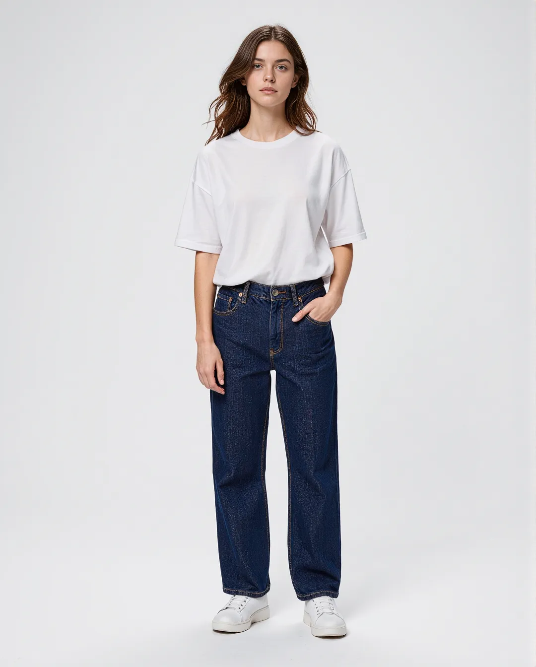 Fashion photograph featuring minimalist styling with oversized white t-shirt tucked into dark straight-leg jeans with white sneakers