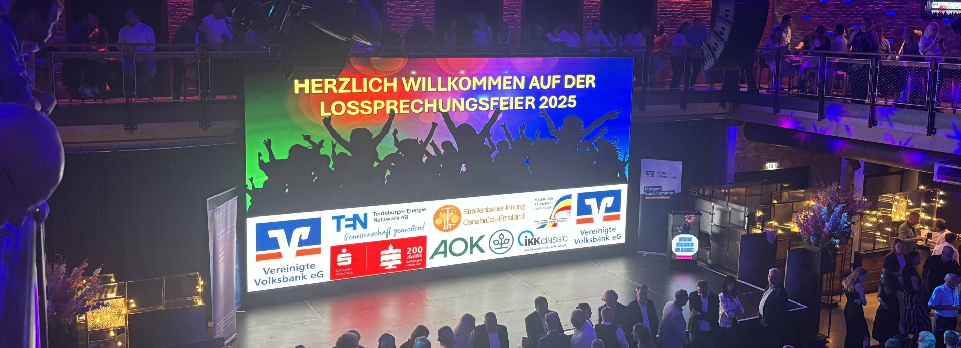 Begrüßung auf der Lossprechungfeier 2025. Willkommen-Banner mit Logos der Sponsoren und begeistertem Publikum im Hintergrund.