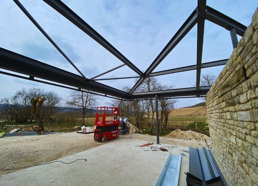 Montage de la charpente métallique sur bâtiment ancien en pierre, avec grue et nacelle sur site.