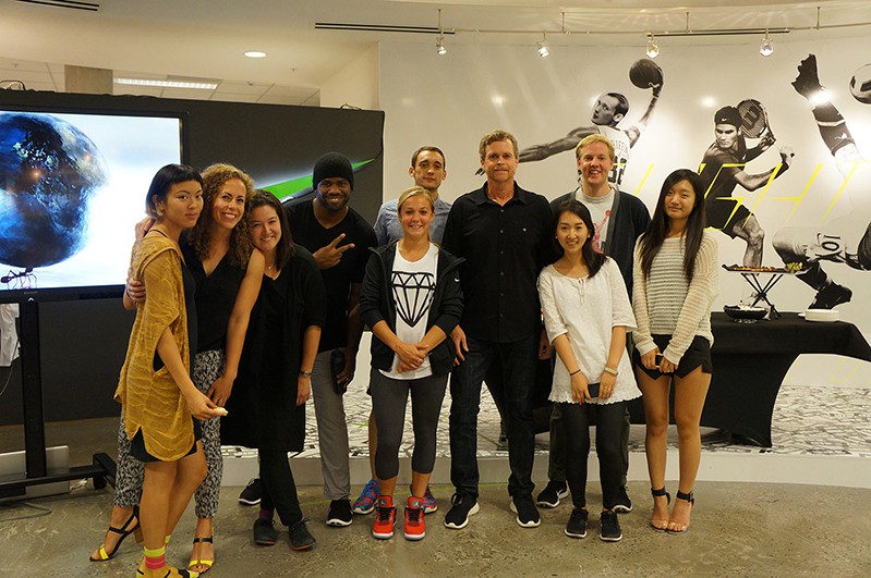 A photo of a group of students in a modern art gallery, near a TV screen.