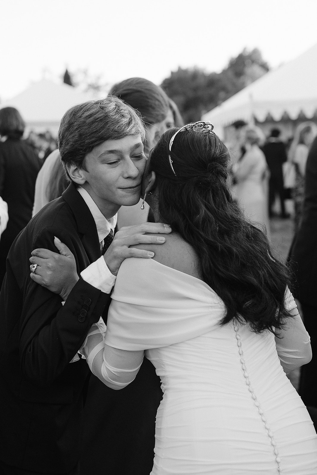A bride in a white dress and a groom in a black suit hold hands, surrounded by greenery in a romantic setting.