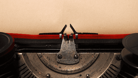 Extreme close-up of a vintage typewriter carriage with a blank page loaded, red ribbon visible against black metal.