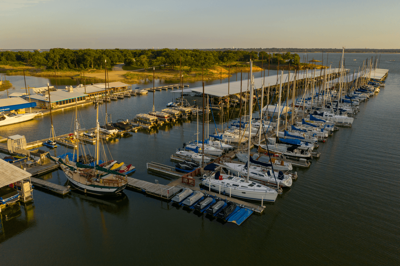 Scenic view of twin coves marina at sunset, featuring numerous sailboats docked on calm water with a backdrop of lush greenery and a clear sky.