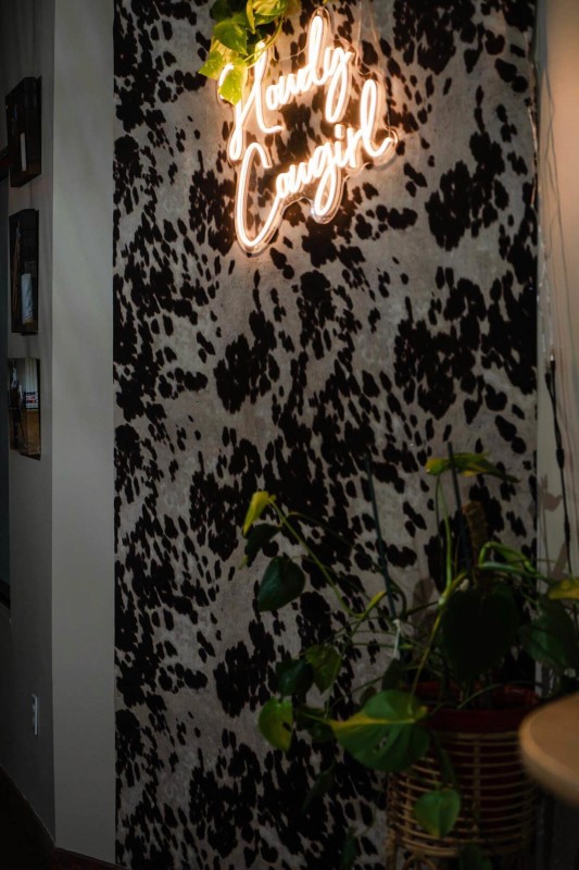 A close-up of a large, hearty chicken wrap or shawarma, filled with meat and fries, generously drizzled with white and orange sauces and sprinkled with parsley, served on a wooden cutting board with a side of French fries.