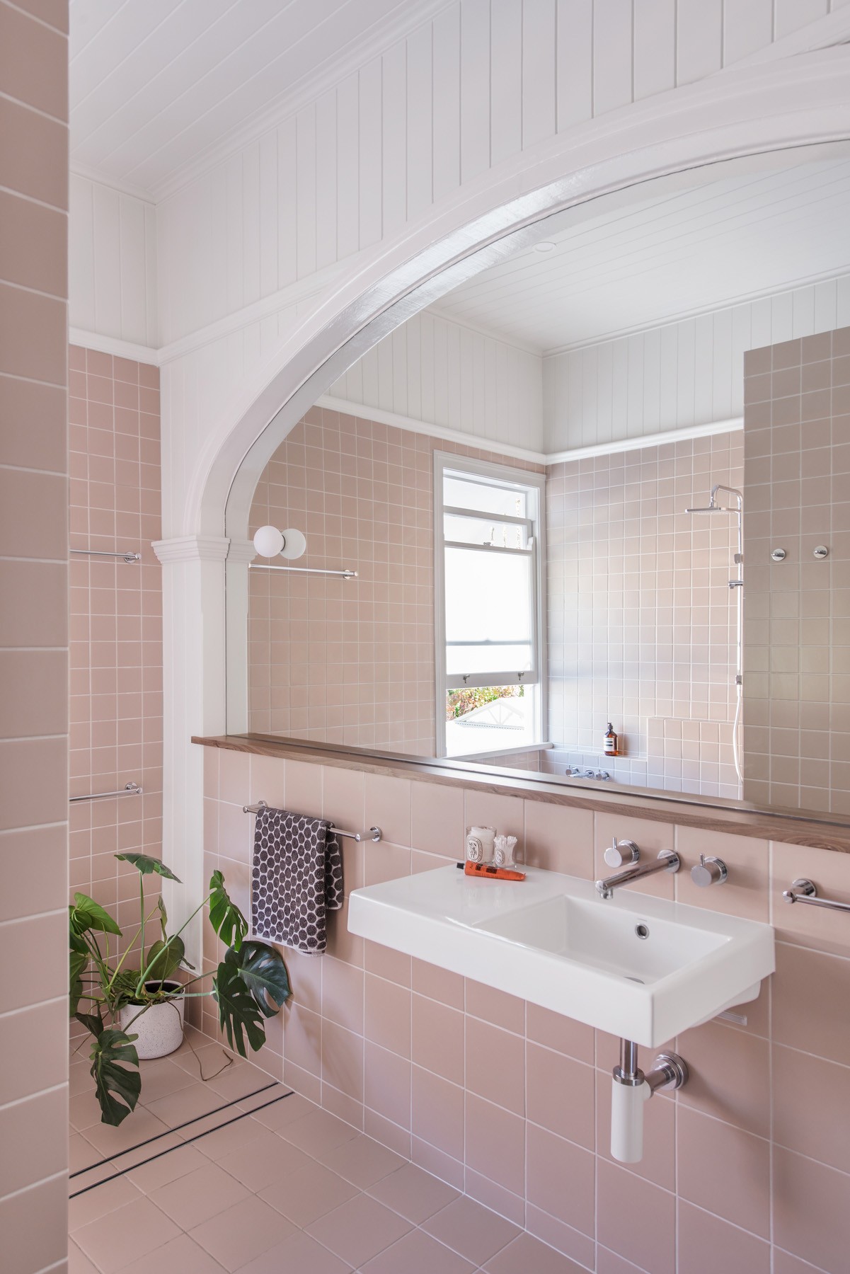 Bathroom vanity within Ridge House with tiled surfaces, an arched mirror opening, and soft natural light filtering through the window.