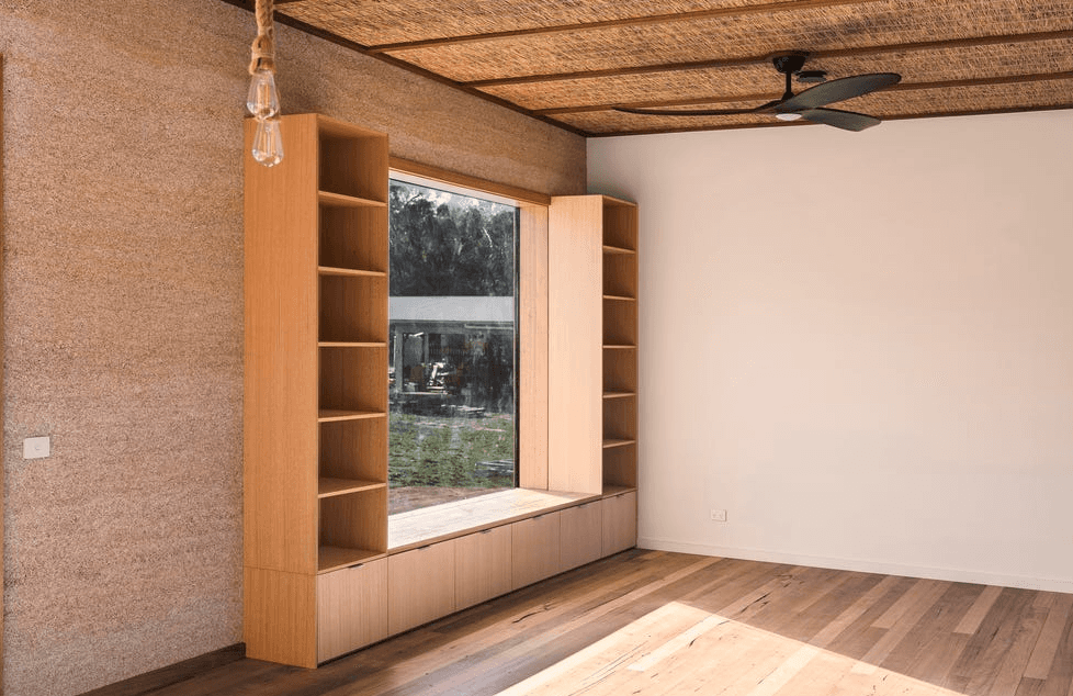 A large window lets in direct sunlight, highlighting the hempcrete block wall.