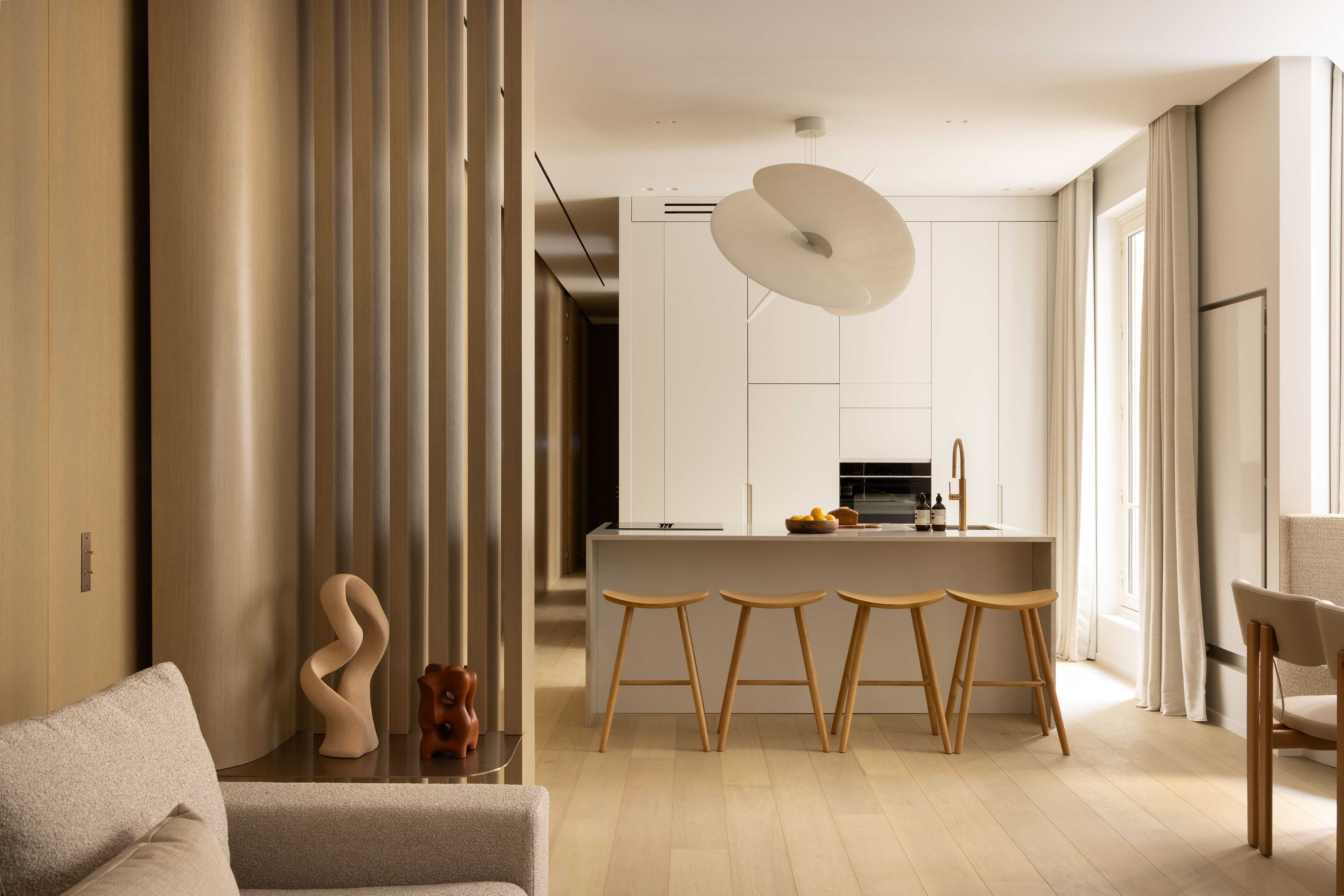 Cuisine ouverte avec îlot central, tabourets en bois, suspension design blanche et claustra
