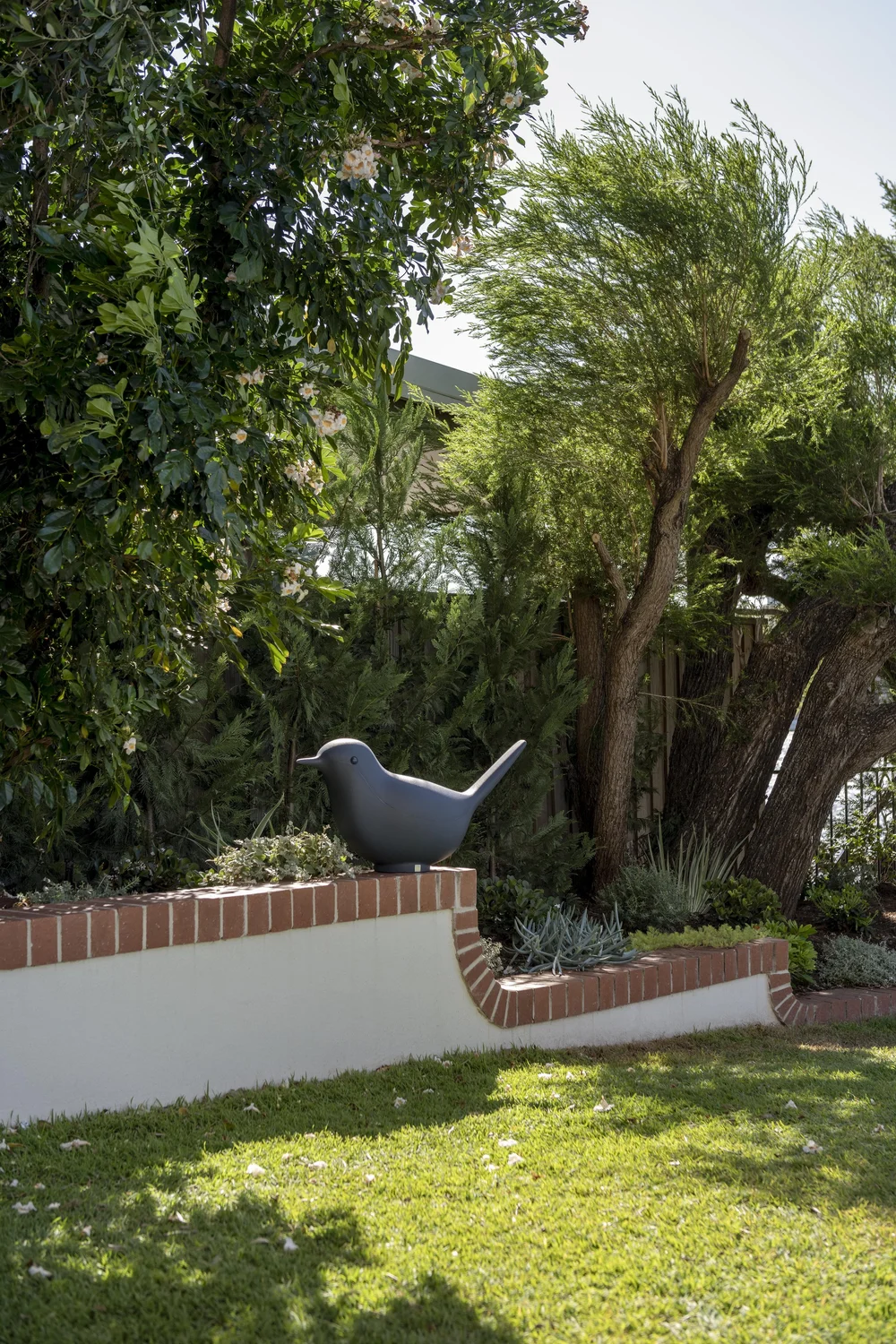 Landscaped garden with brick-edged planter, lush greenery, and a sculptural black bird feature.