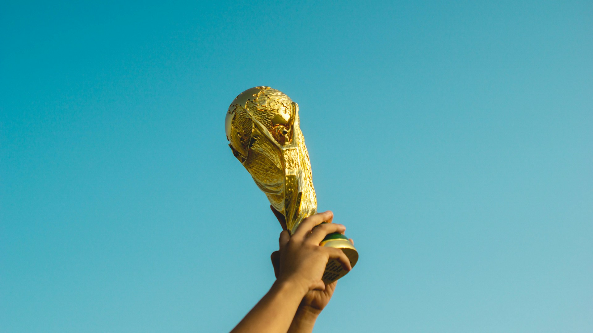 The World Cup trophy being hoisted into the air against a clear blue sky.