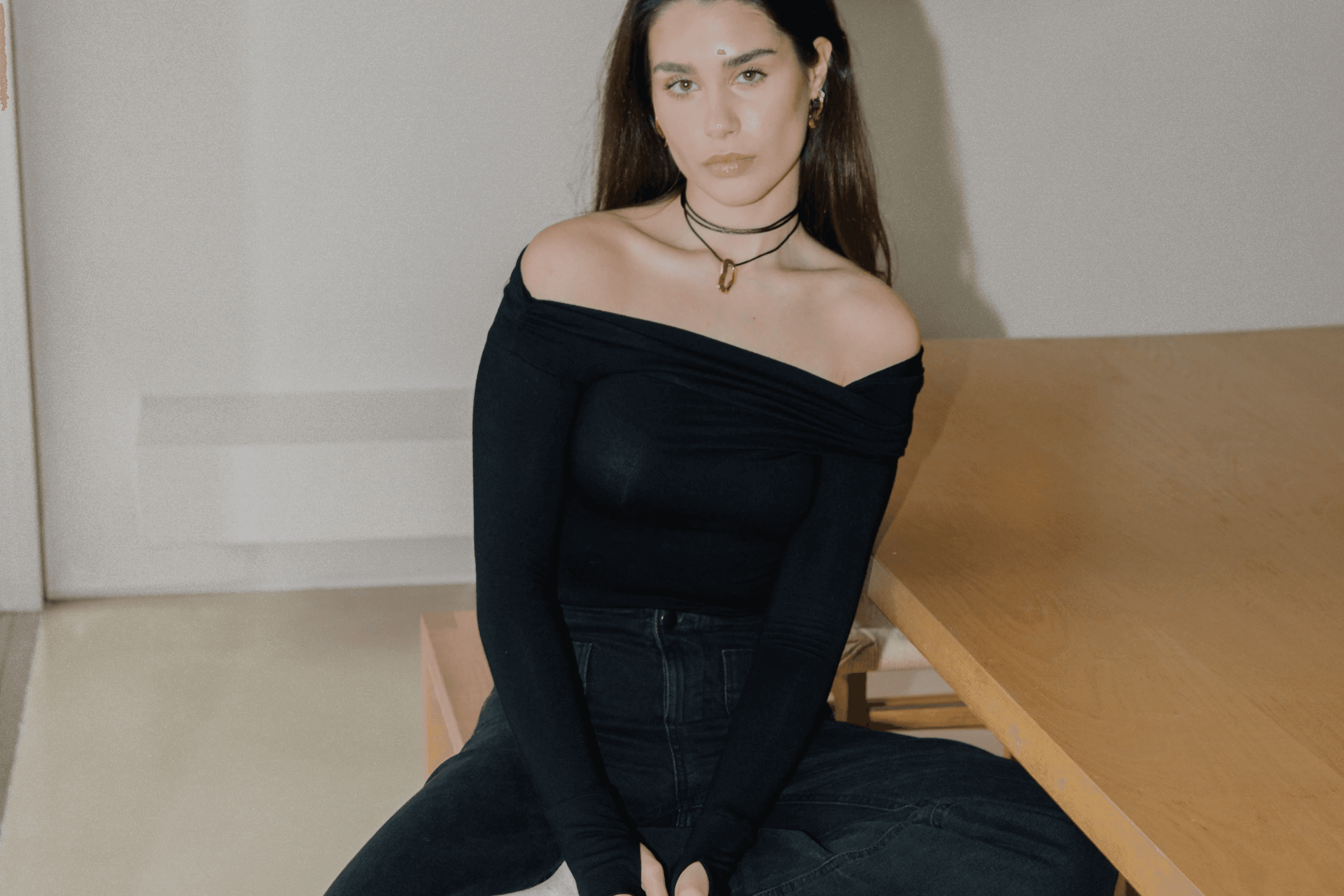 Woman in dark clothing sitting on floor with light hair and necklace on.