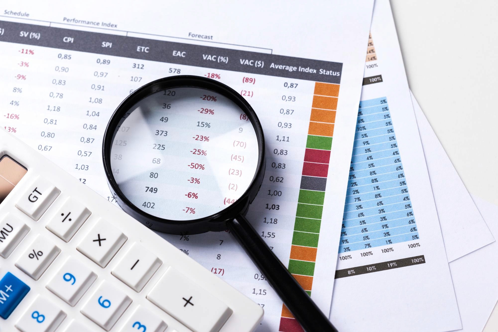 A black magnifying glass resting on data sheets next to a white calculator.