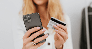 Closeup of a woman's hands - one holds a cell phone and the other holds a credit card.