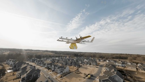 A person wearing blue medical gloves holds a test tube near a computer keyboard on a laboratory desk, with hospital documents and laboratory equipment in the background.