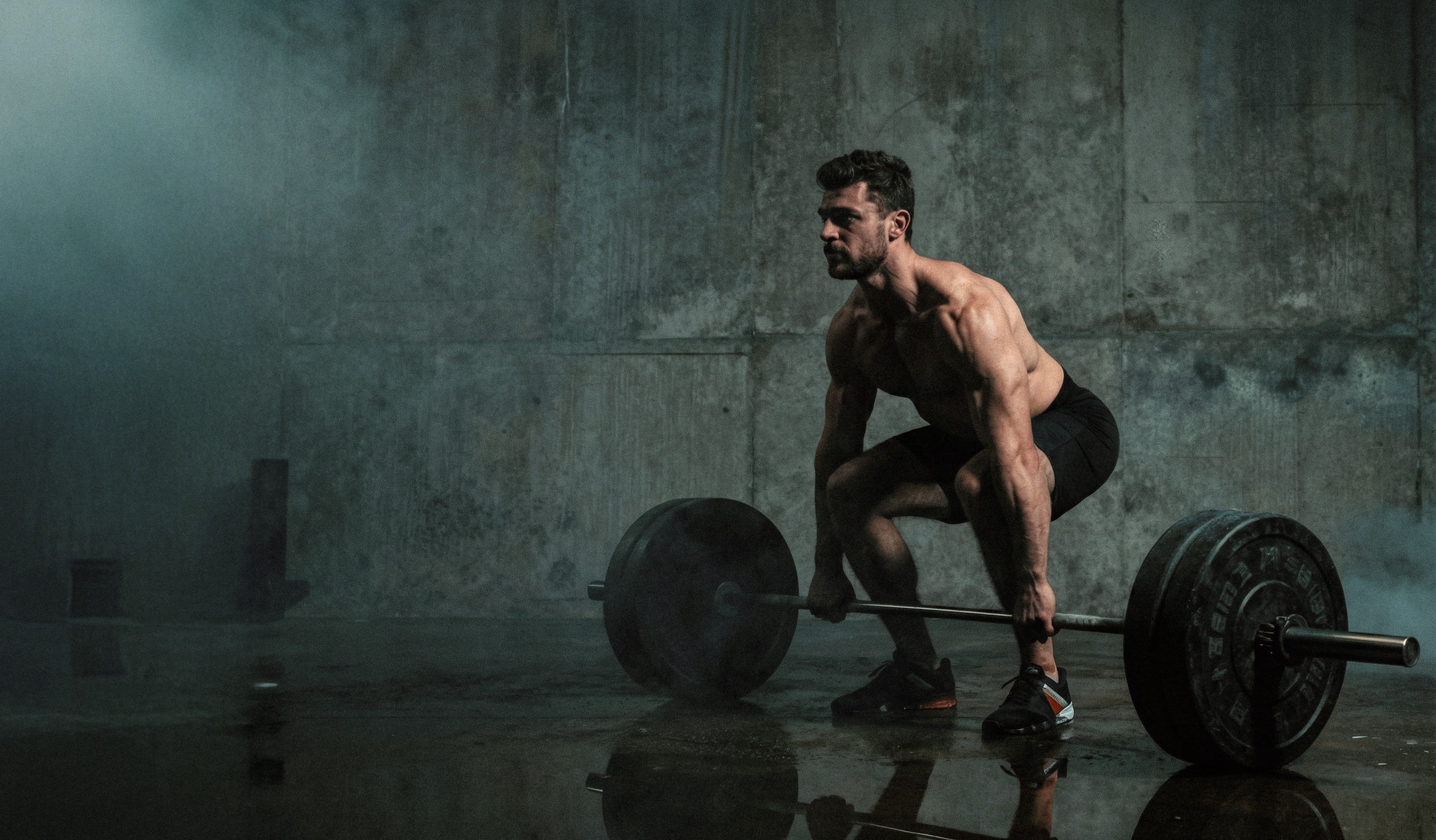 A personal coach lifts a heavy barbell in a dimly lit gym, focusing intently on the task.