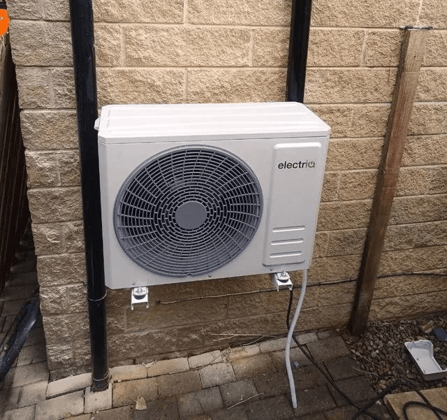 Wall-mounted air-to-air heat pump indoor unit in a UK living room providing both heating and cooling