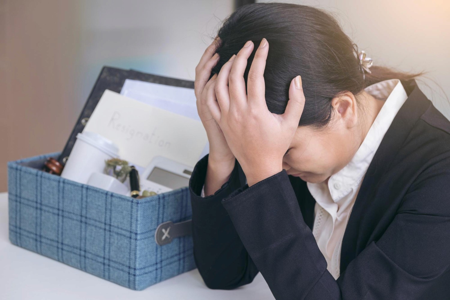 穿著深色西裝的女性因離職感到沮喪，身旁放有辦公室整理盒及離職信，涉及香港僱員補償保險及勞工保障範疇。