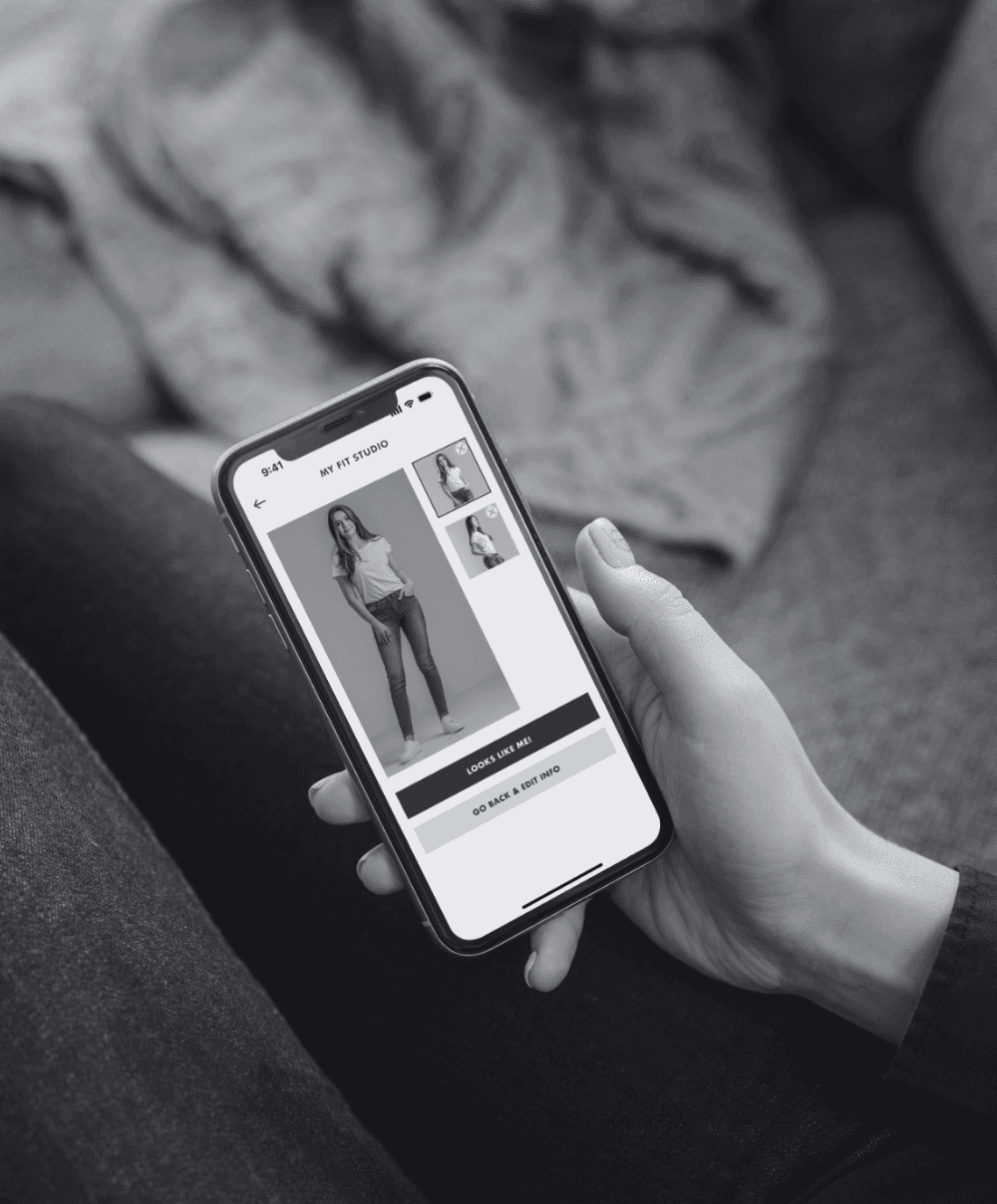 A person holds a smartphone, viewing an online shopping app displaying clothing items, including images of a model in jeans.