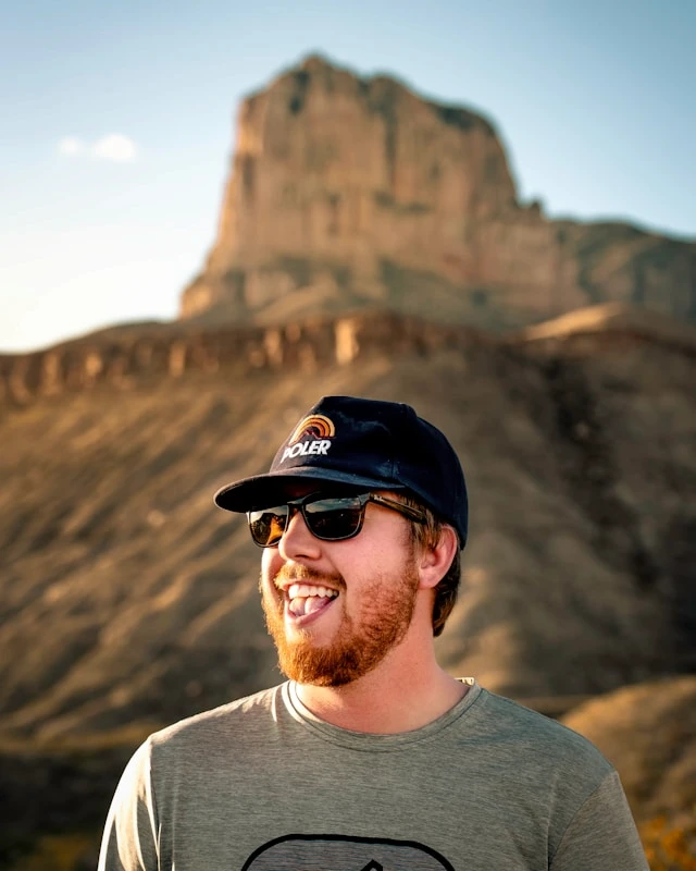 Smiling man outdoors in warm sunlight wearing sunglasses and a cap