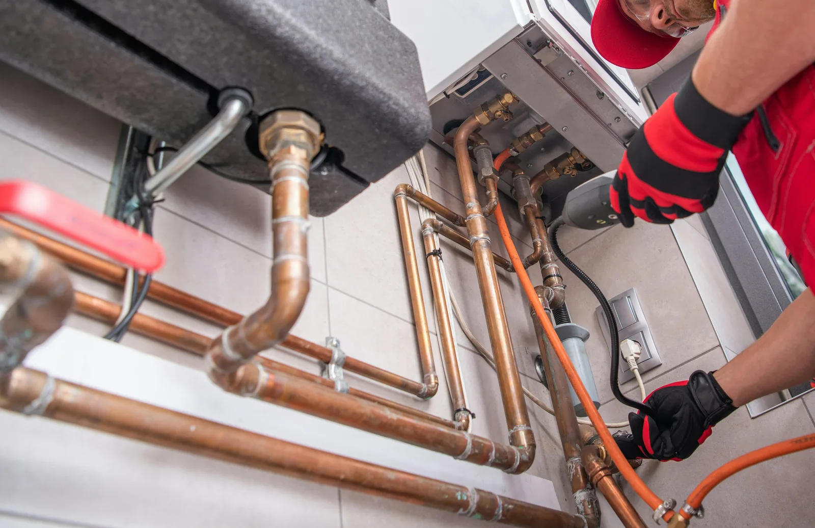 Technician in red uniform servicing copper pipes and boiler system