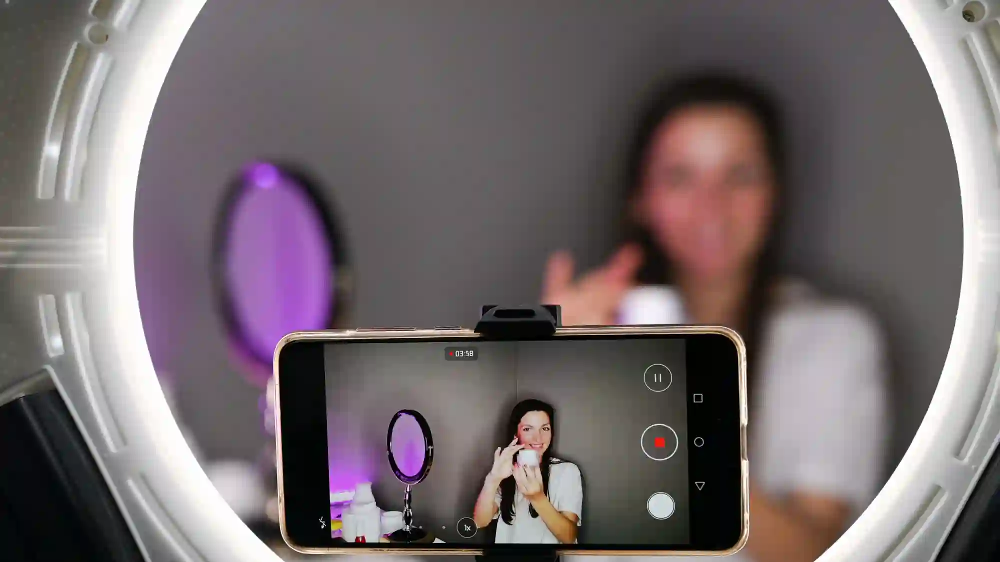 A phone recording a woman speaking into a microphone with a ring light.