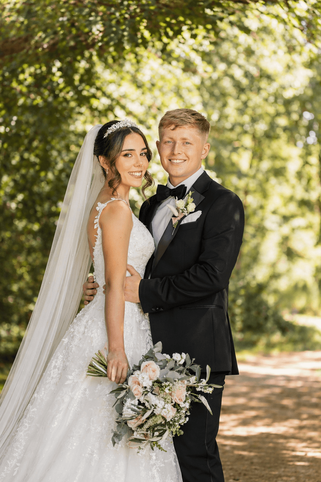 Wedding portrait: Bride in lace gown, veil, and tiara, holding bouquet. Groom in black tuxedo.