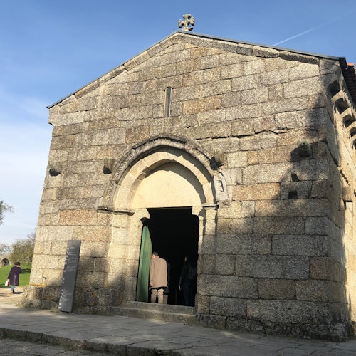 石造建築，帶有拱形入口，門口旁有幾個部分可見的人物，背景是晴朗的天空。