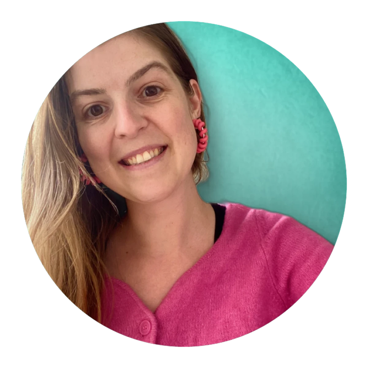 Person with long hair wearing a bright pink top and pink earrings against a teal background.