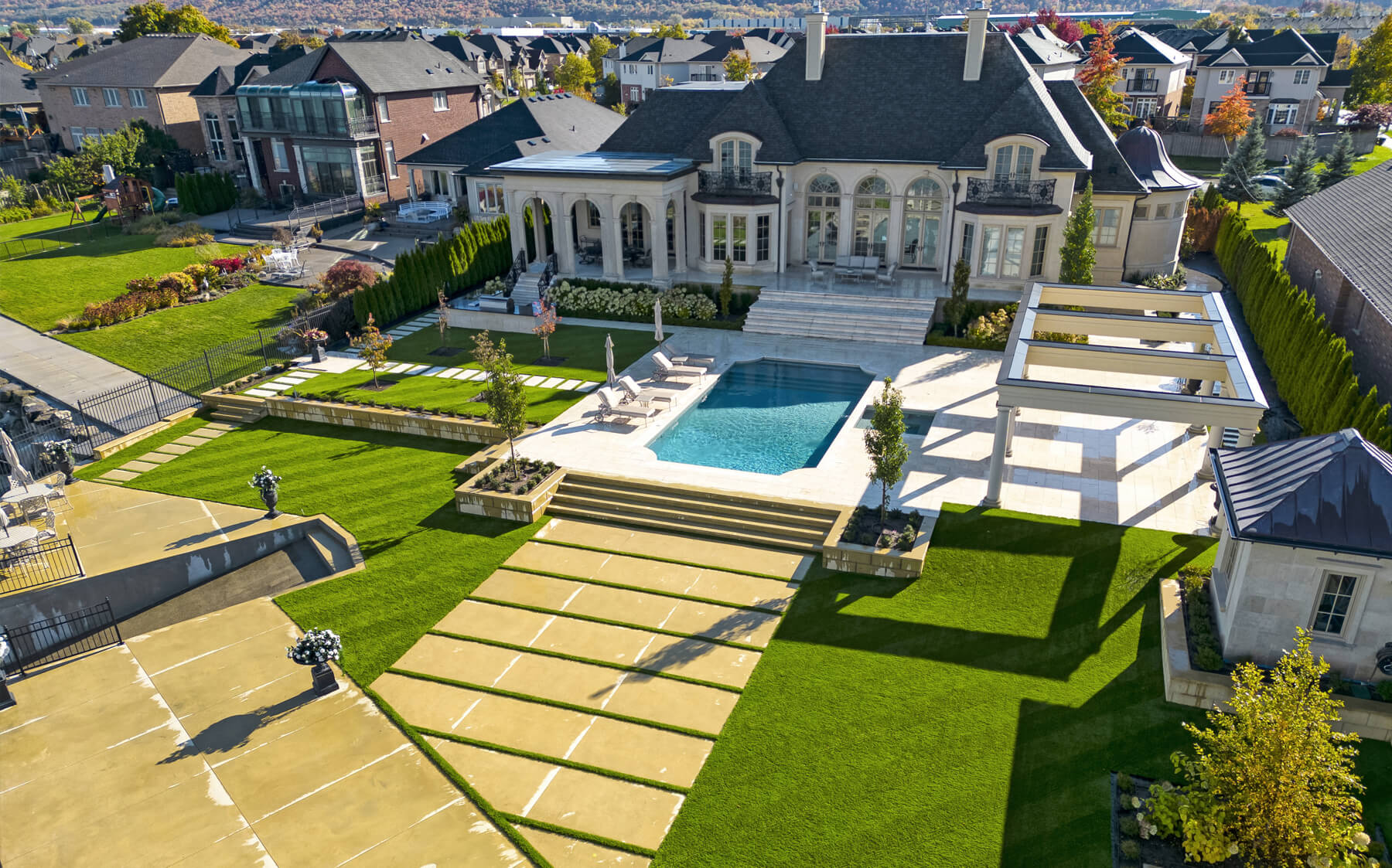 A large house surrounded by a green AGL Grass North artificial lawn featuring a sparkling blue pool in the backyard.