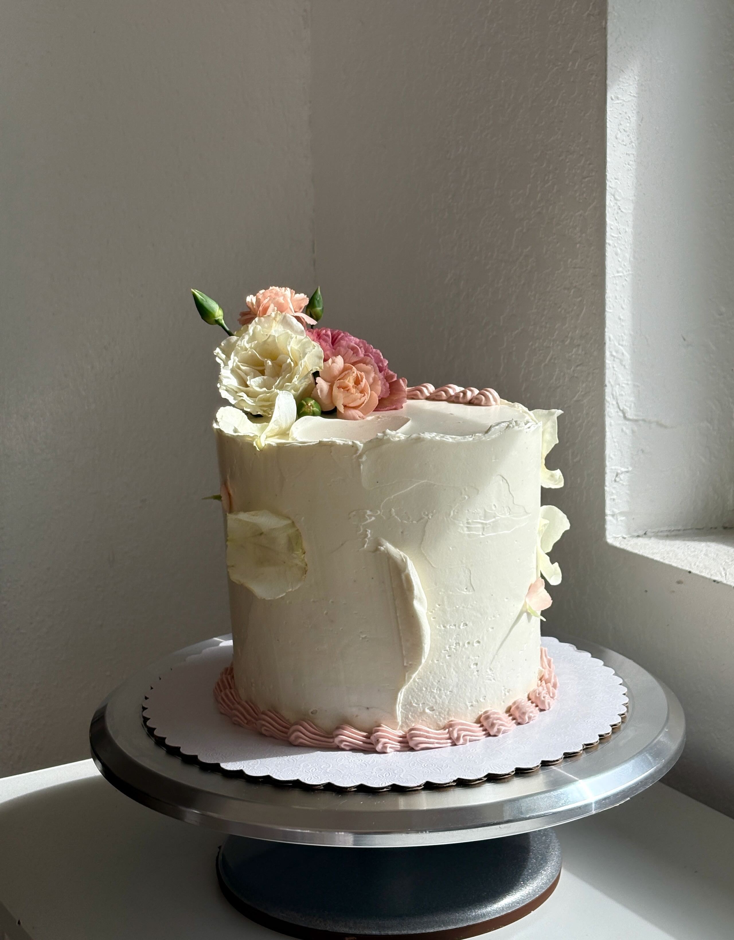 White plate with roasted carrots served on green sauce, topped with almonds and fresh herbs, held by a hand over a dark table.