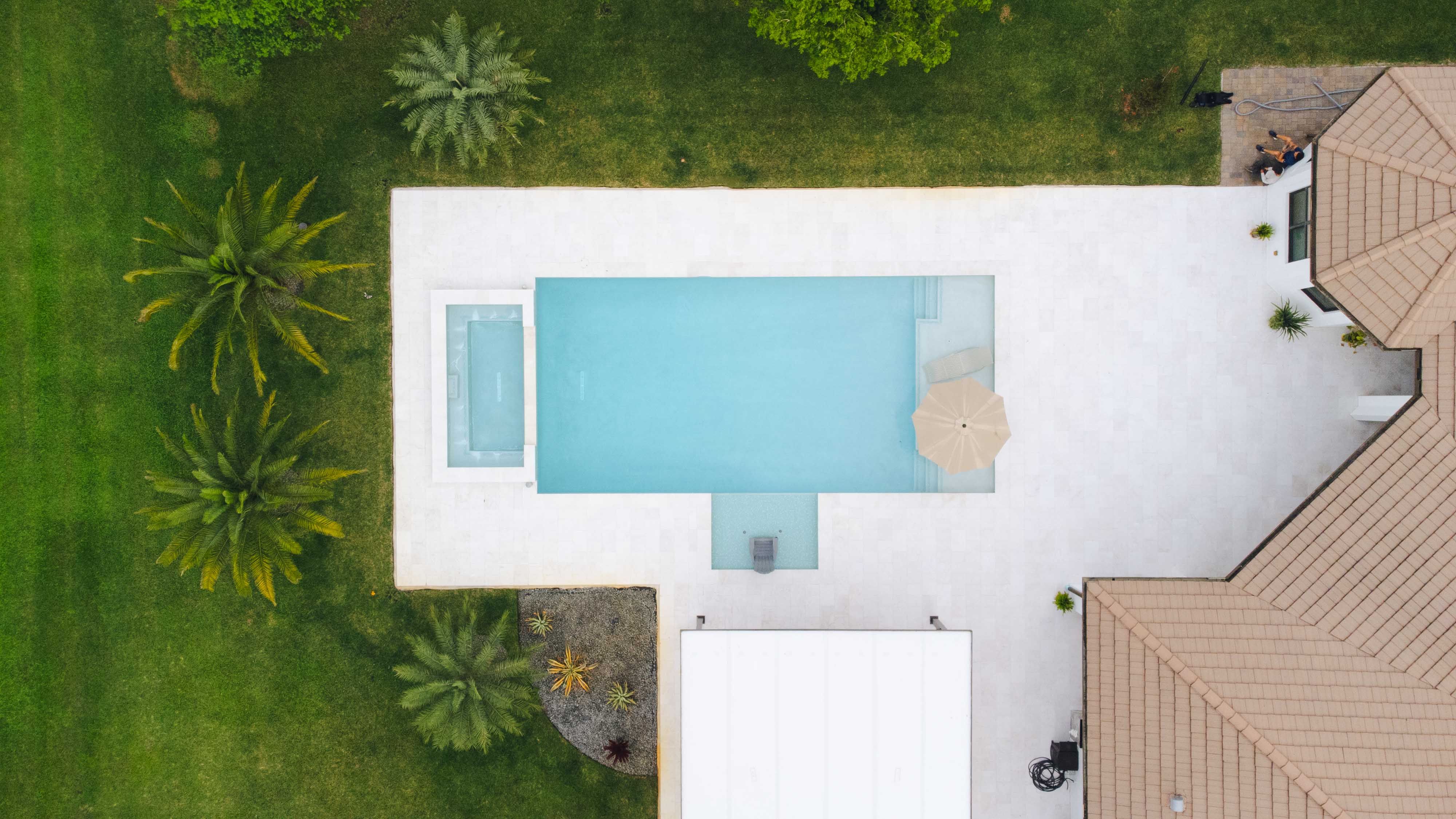 Aerial view of a modern backyard with a rectangular pool, spa, and tan umbrella.