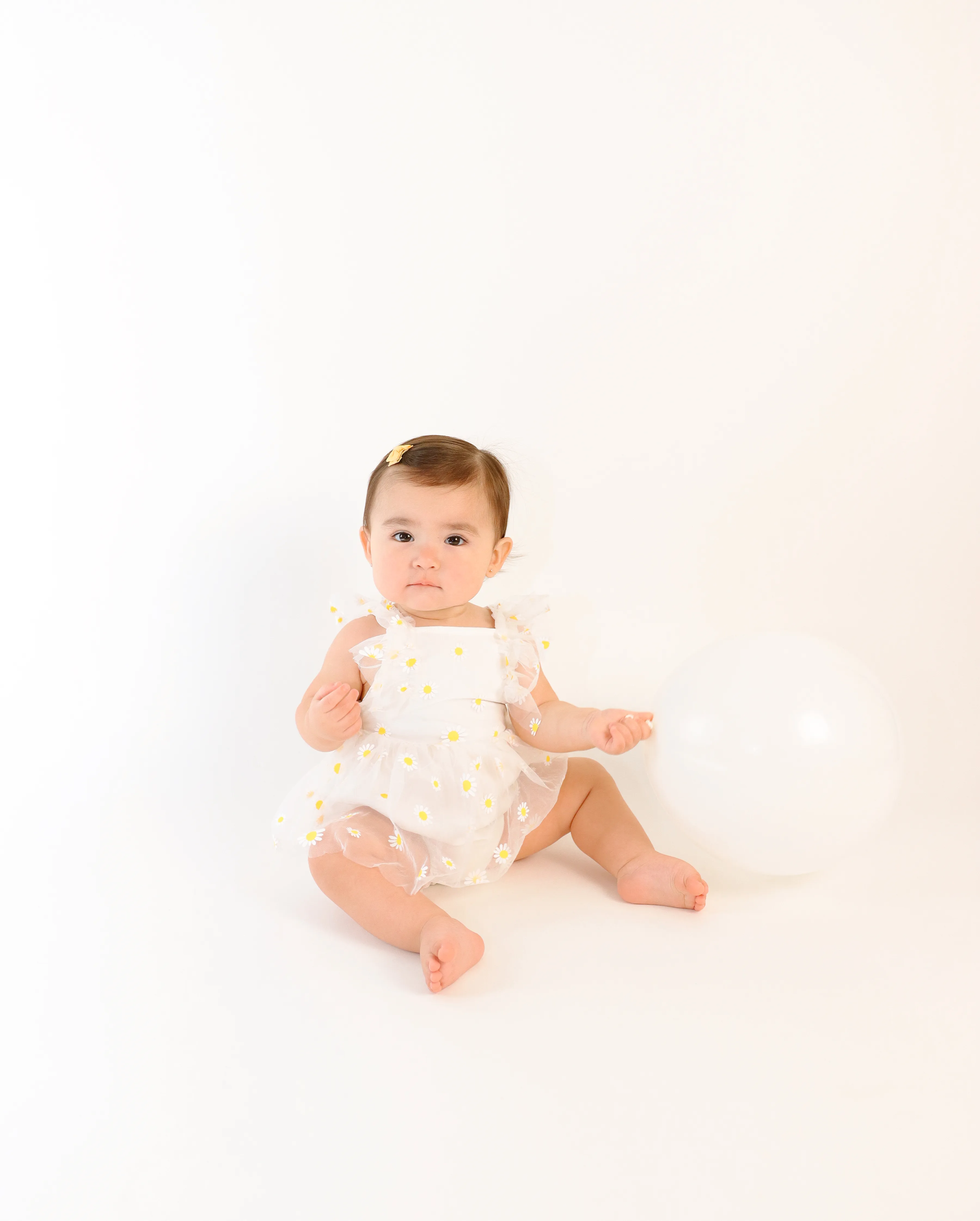 Retrato infantil de bebé sentada junto a un globo blanco