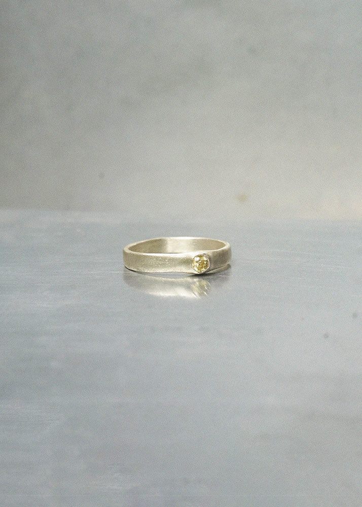Silver ring with a small yellow gemstone on a gray surface