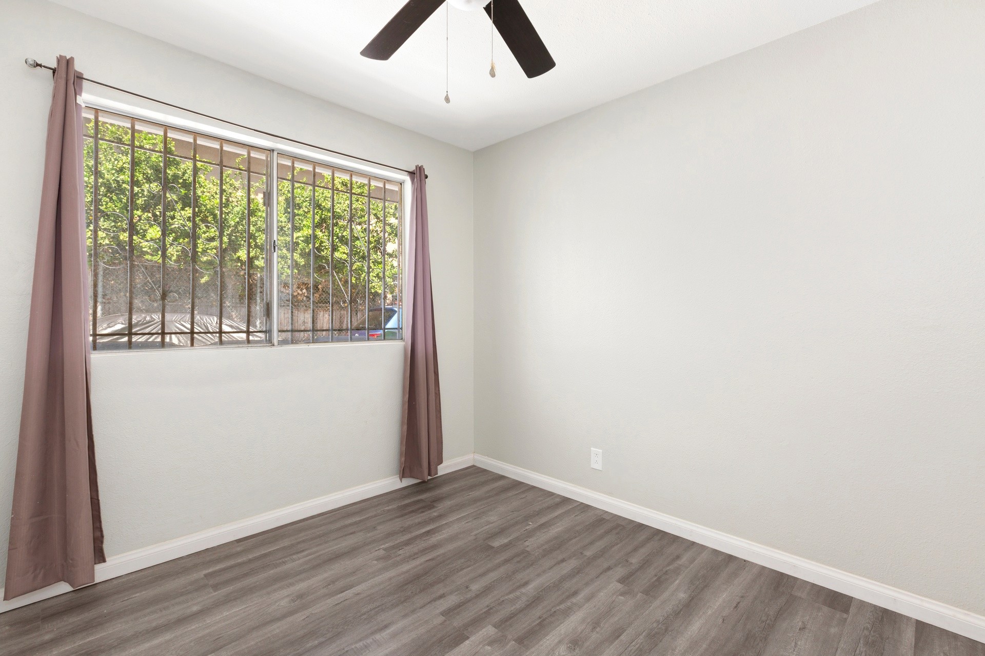 A well-lit empty room at 4421 Wall, features hardwood floors, a ceiling fan, and windows with sheer curtains.