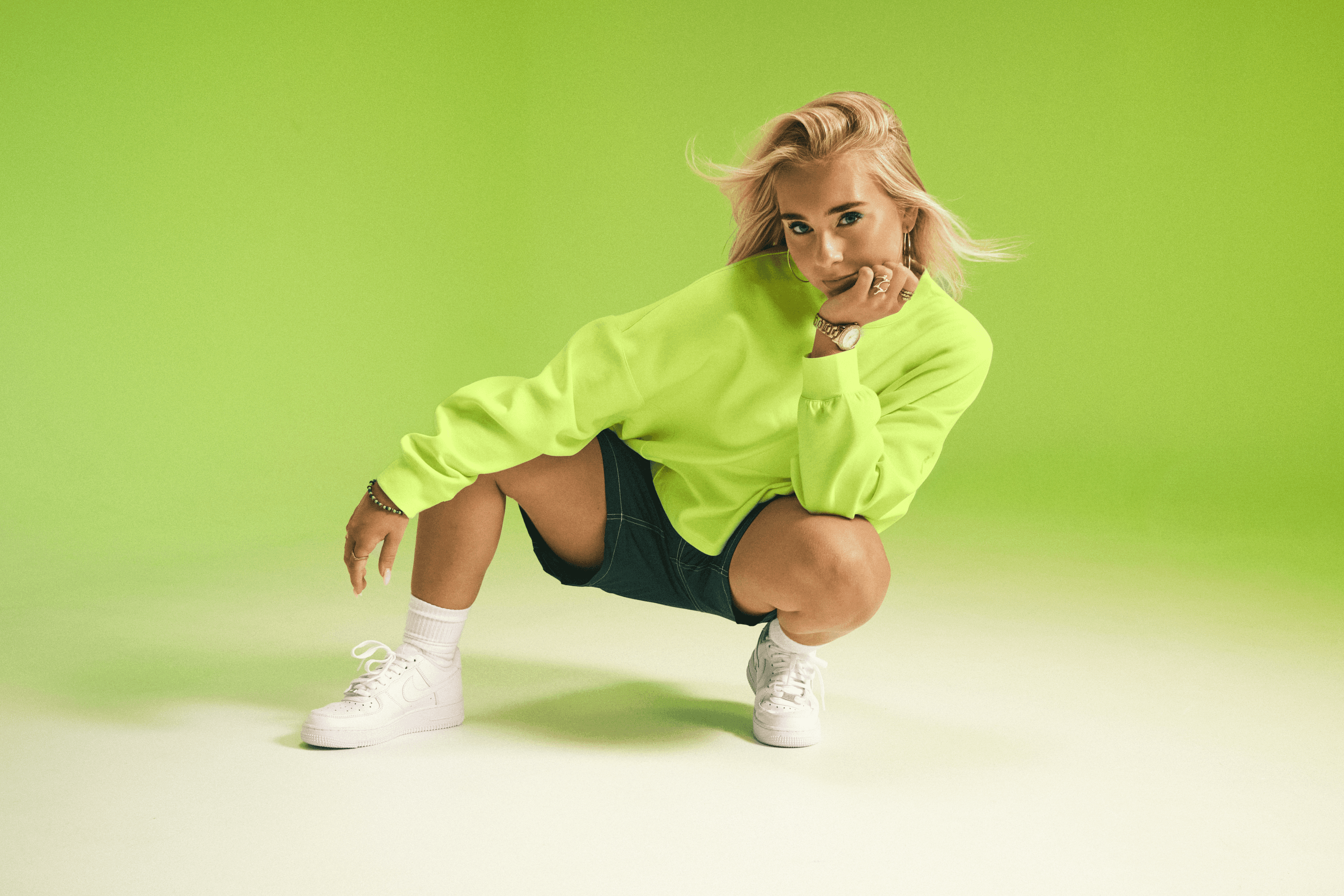 Model in a lime green sweatshirt crouching against a lime studio backdrop