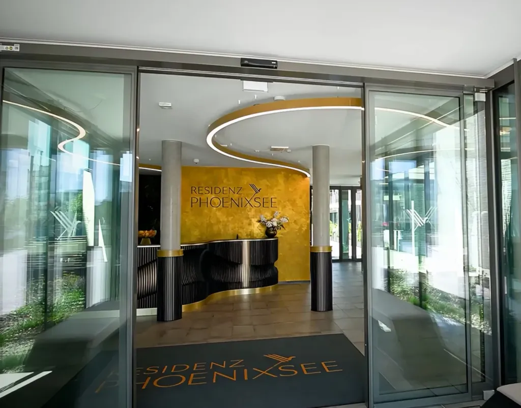 Modern lobby entrance with glass doors, white ceiling, contemporary lighting, and yellow accent wall