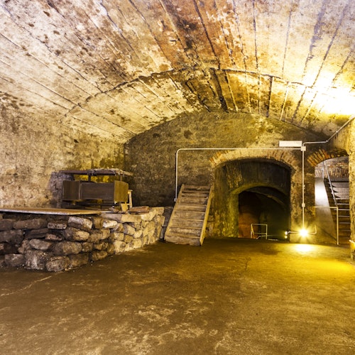 一个带有拱形天花板、楼梯、带机械的高台和昏暗灯光的老石地窖。