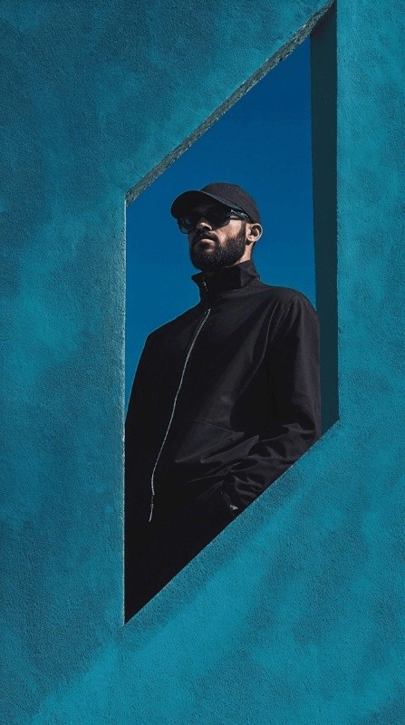 Man in a black high-neck top against a vibrant blue textured wall