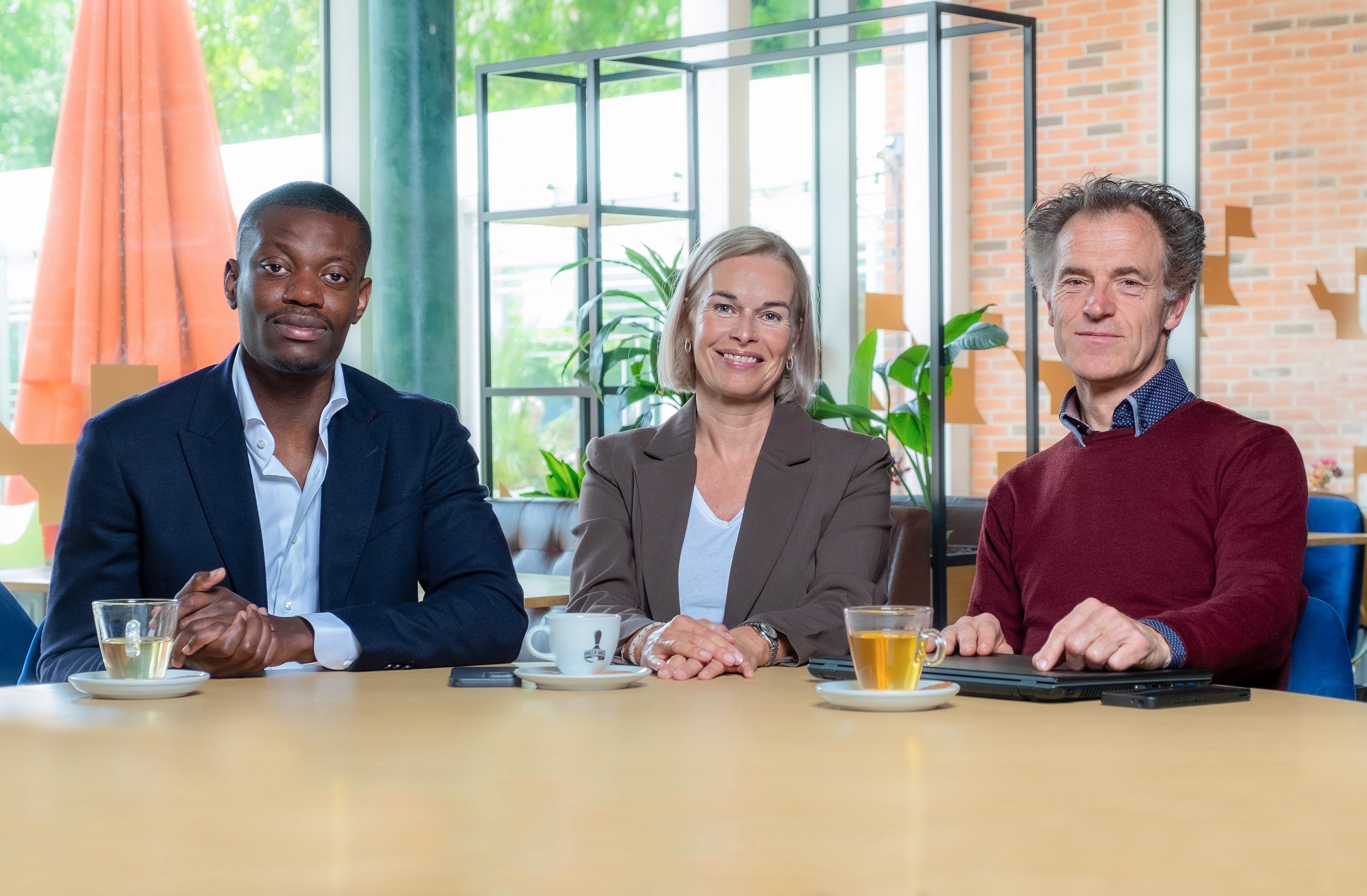 Drie teamleden van ADCM kijken lachend in de camera tijdens een informele fotosessie op kantoor, met een warme en toegankelijke uitstraling.