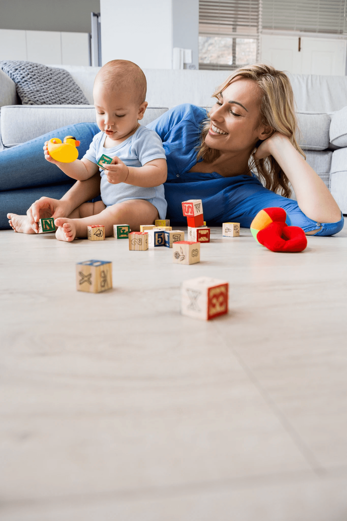 A mother and baby playing with toys on light wood-look hybrid flooring, highlighting LUXO Floors’ safe, waterproof, and family-friendly hybrid floors designed for modern Australian homes.