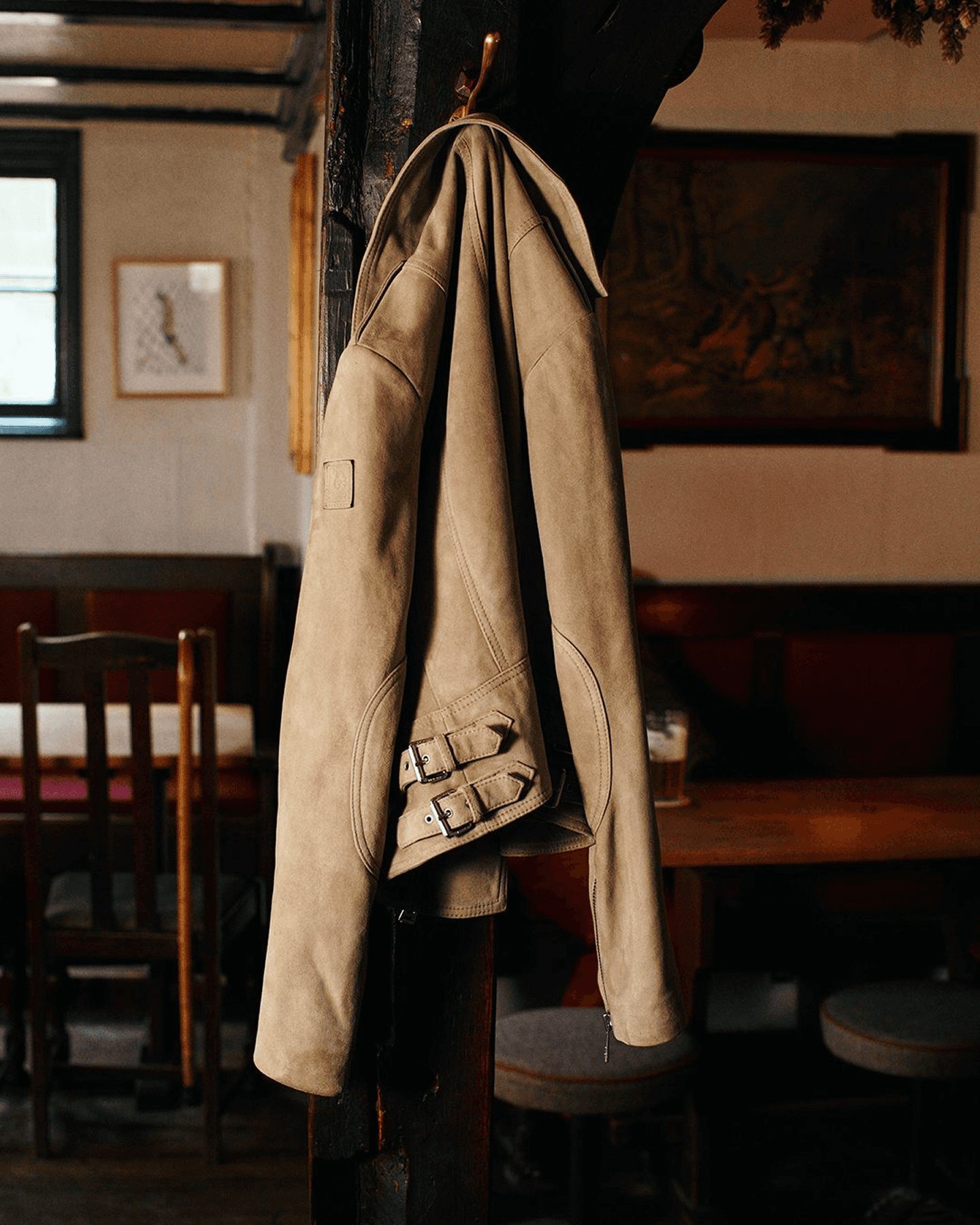 Un blouson biker en daim beige Belstaff pour femme est accroché à un clou dans un pub