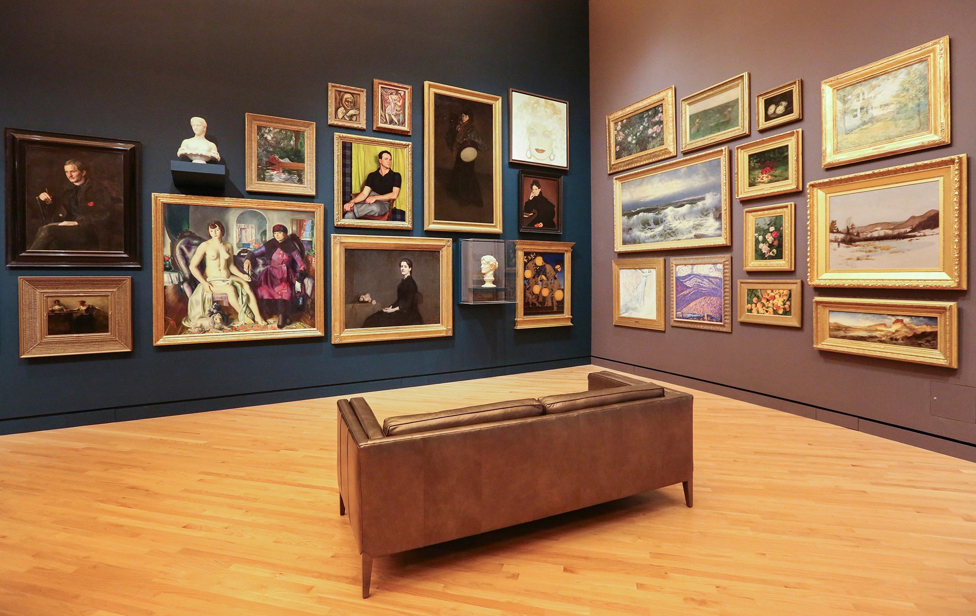 A museum room with a collection of framed paintings in gold frames on a dark wall