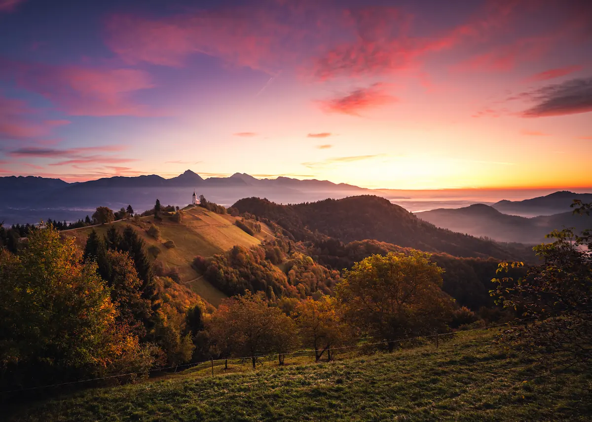 A stunning sunset over rolling hills at Jamnik, Slovenia, with vibrant clouds and warm light illuminating the landscape.