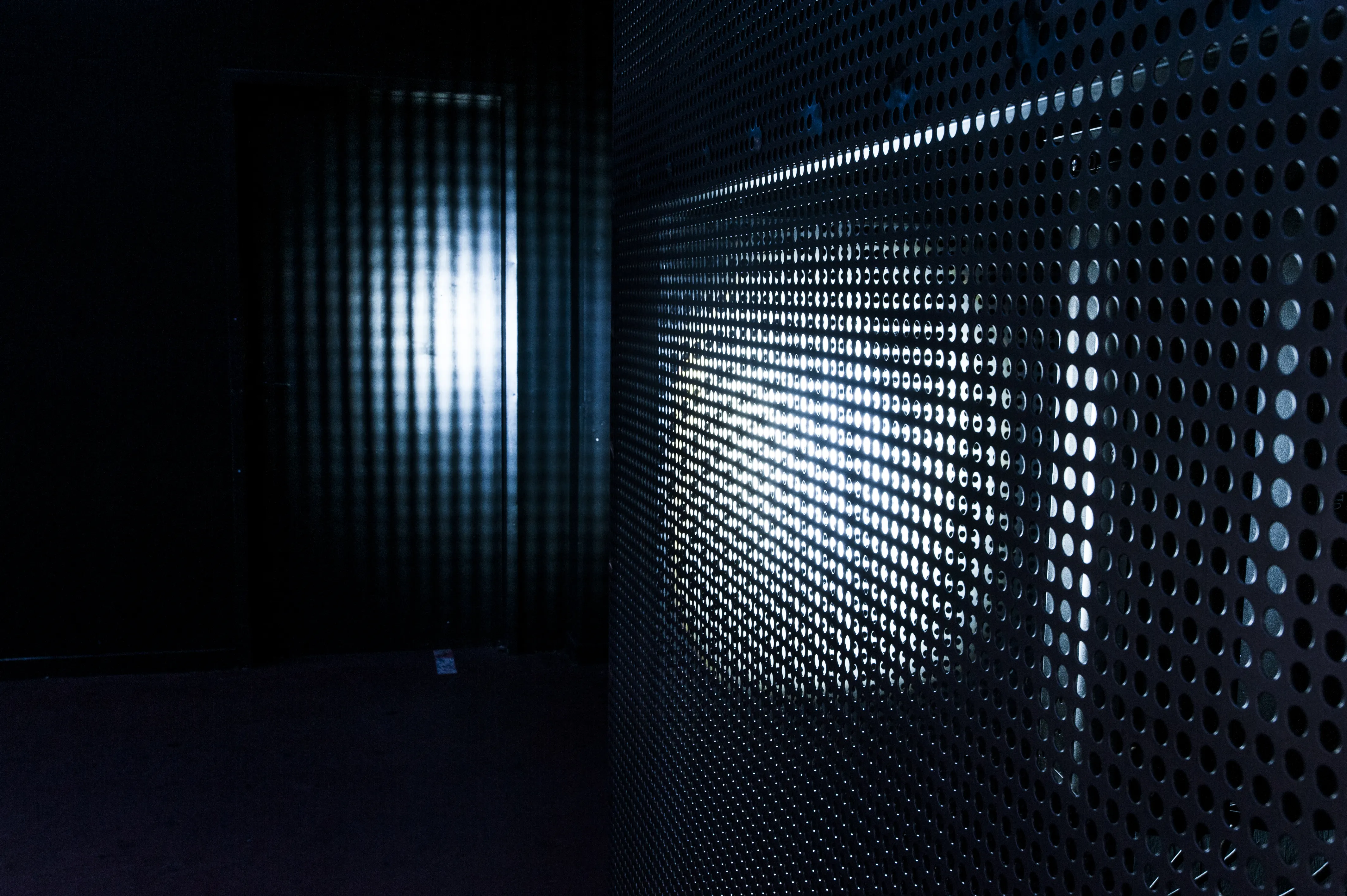 Light beam shining through a perforated metal wall in the dark interior of the Jägermeister Night Embassy.