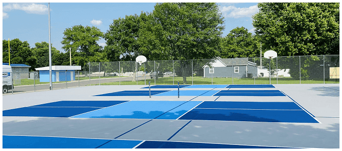 Blue and gray outdoor pickleball courts with precision-applied acrylic surface and basketball court nearby