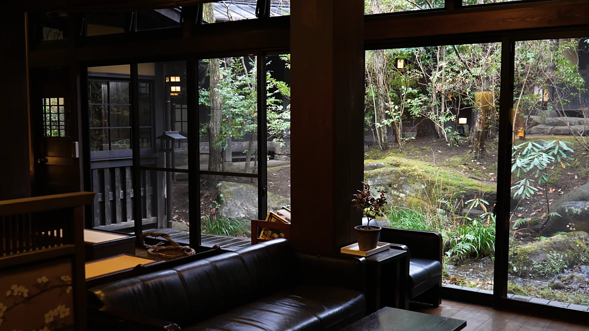 A ryokan lounge at Kurokawa Onsen with leather seating and full-height windows onto a garden