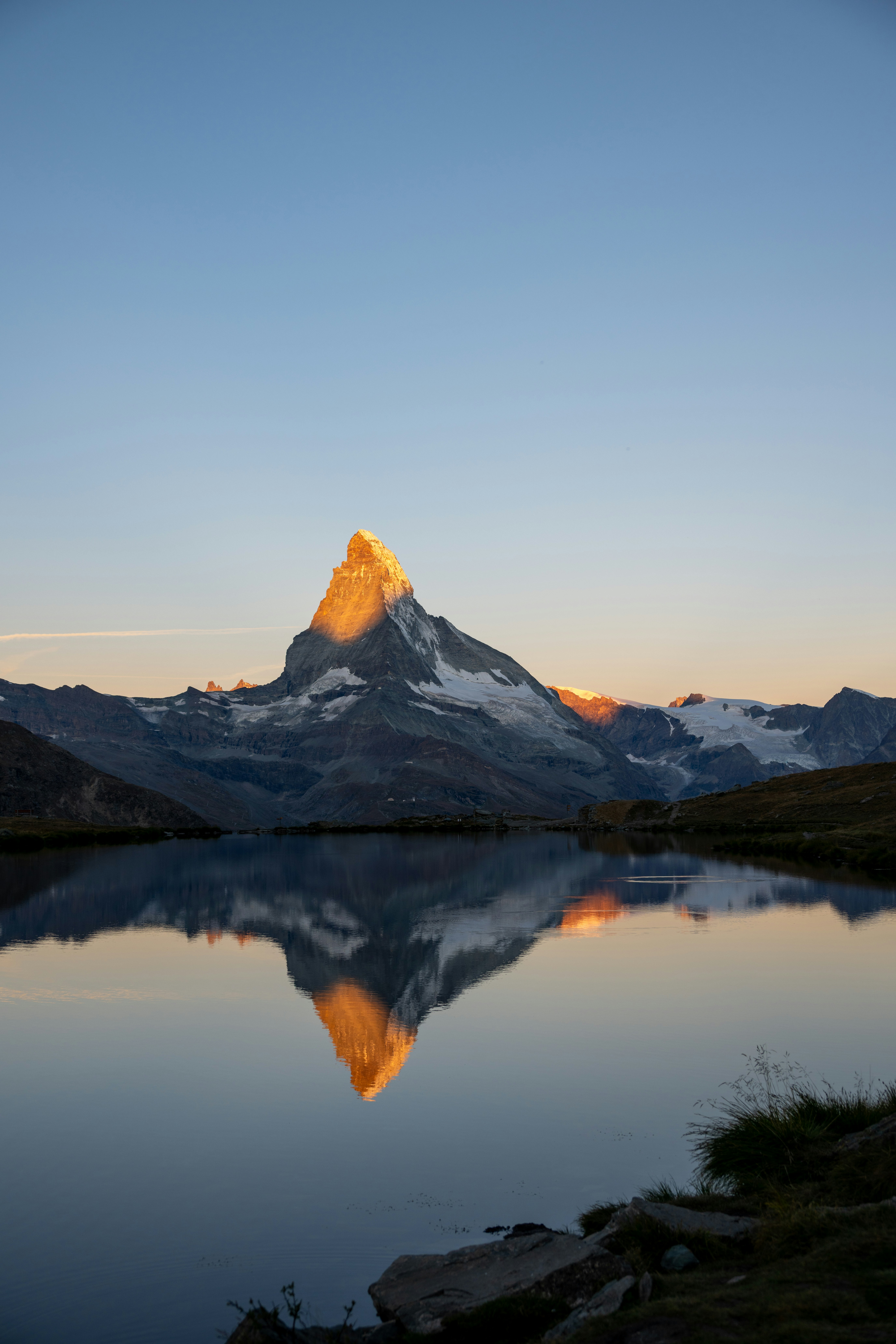 Mountain peak reflecting in calm lake at sunrise.