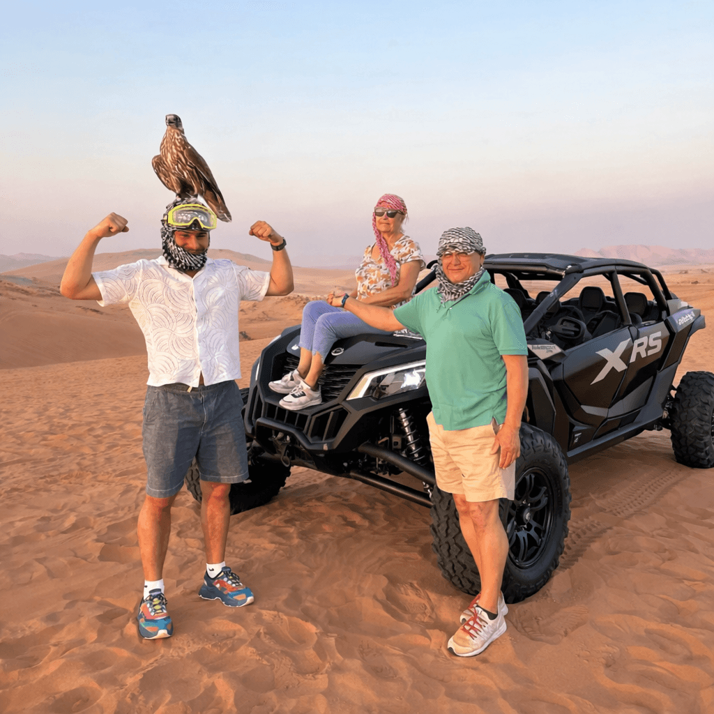 Family posing with falcon beside Can-Am Maverick X3 dune buggy during Dubai desert safari with Dune Quest Tours